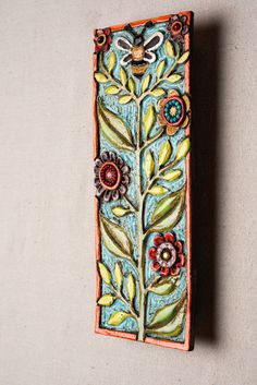 a decorative wall hanging made out of ceramic with flowers and leaves painted on the side