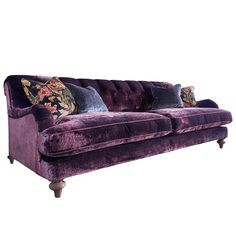 a purple velvet couch with floral pillows on the armrests and back rests against a white background