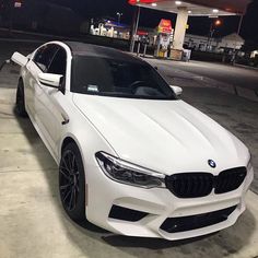 a white bmw is parked in front of a gas station at night with the lights on