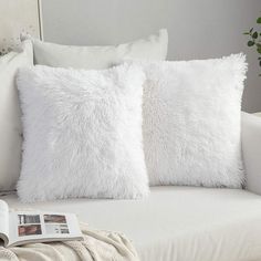 two white pillows sitting on top of a couch next to a pillow with a magazine