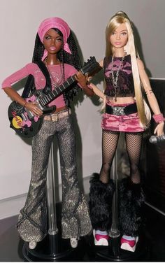 two barbie dolls standing next to each other on a black table with guitars in their hands