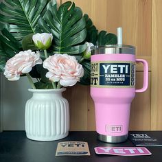 a pink yeti tumbler next to a white vase with flowers in it on a table