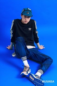 a young man sitting on the ground wearing adidas shoes