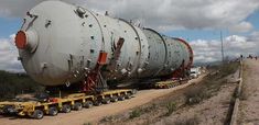 a large metal object being loaded onto a flatbed truck on the side of a dirt road