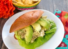 a sandwich with lettuce and avocado is on a plate next to chips