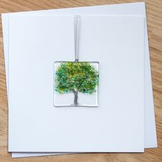 a card with a tree in the middle and green leaves on it, hanging from a string