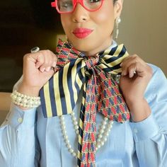 a woman wearing red glasses and a blue shirt with a striped scarf around her neck