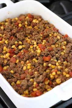 a white casserole dish filled with ground beef, corn and tomatoes on the side