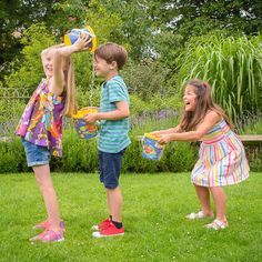 three young children playing in the grass with frisbees and water juggling