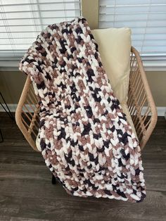 a brown and white crocheted blanket sitting on top of a wooden chair next to a window