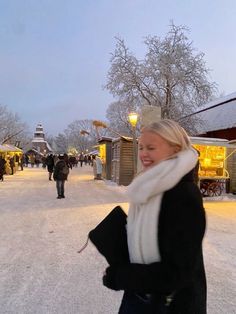 a woman smiles as she walks through the snow in front of buildings and shops at night