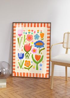 an orange and white flowered painting sitting on top of a wooden floor next to a chair