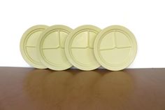 three yellow plastic plates sitting on top of a wooden table next to a white wall