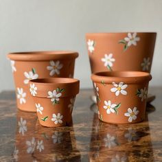 four clay flower pots with white flowers painted on them sitting on a marble table top