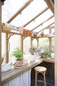 an indoor greenhouse with plants and potted plants on the shelves, along with a stool