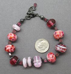 "In the mood for pink? Then this bracelet fits perfectly! It features a selection of my handmade pink lampwork beads. The colors range from dark translucent pink, pink and purple frit beads, to light pink swirls. These beads are simply stunning! Such a beautiful combination for Spring! The beads are strung along side sterling silver flower bead caps and pink Tourmaline rectangle shaped gemstone beads. I have made the lampwork beads in this bracelet. The sterling silver has been oxidized to add d Bohemian Pink Beaded Bracelets Czech Glass, Pink Bohemian Beaded Bracelets In Czech Glass, Bohemian Pink Beaded Bracelets From Czech Glass, Pink Round Beaded Bracelets With Spacer Beads, Pink Bracelets With Large Beads For Jewelry Making, Adjustable Pink Bracelets, Adjustable Pink Glass Bracelets, Pink Glass Beaded Bracelets As Gift, Handmade Pink Glass Bracelets