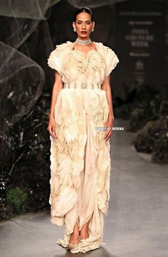 a model walks down the runway in a white gown with feathers on her head and shoulders