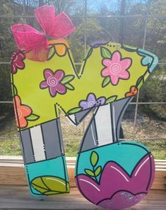 a large letter made out of paper with flowers and leaves on the letters is sitting in front of a window