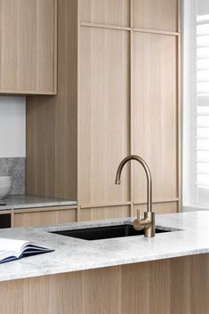 a kitchen with wooden cabinets and marble counter tops, an open book on the sink