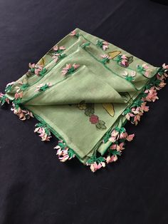 two green napkins with pink flowers on them sitting on a black table cloth,