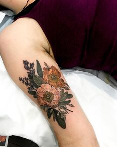 a woman's arm with flowers and leaves tattooed on her left arm, sitting on a bed