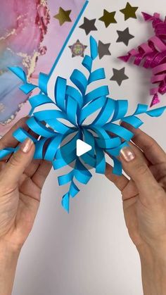 two hands holding up a blue paper snowflake with stars on the top and bottom