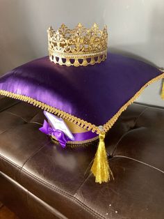 a purple pillow with a gold crown on it sitting on a brown leather bench in front of a gray wall