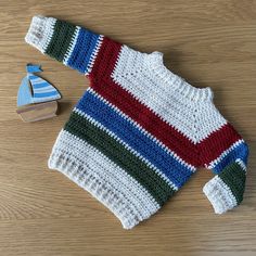 a crocheted sweater next to a wooden toy boat on top of a table