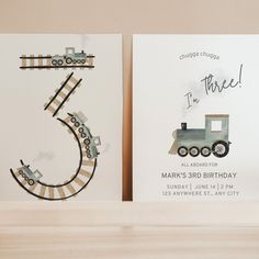 two birthday cards with trains on them sitting on top of a wooden shelf next to each other