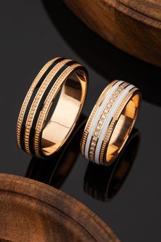 two gold rings with white and black bands on top of a wooden barrel in front of a dark background