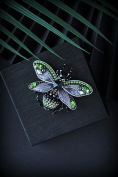 a green and black insect brooch sitting on top of a piece of paper