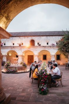 a group of people sitting around a table with flowers on it in front of an archway