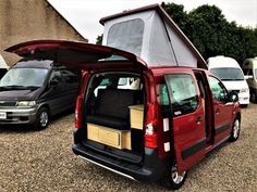 a red van is parked next to other vans in a parking lot with its doors open