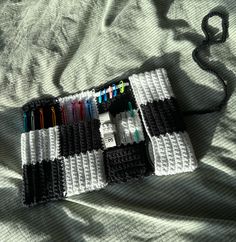 a black and white crochet bag with pens and markers in it on a bed