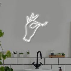 a bathroom sink under a neon sign with a hand coming out of the faucet