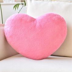 a pink heart shaped pillow sitting on top of a white couch