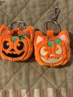 two orange cat keychains with faces on them sitting on a quilted surface