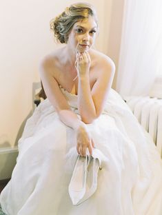 a woman in a wedding dress sitting on a bed with her hand to her face