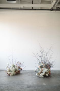 three vases filled with flowers sitting on top of a cement floor next to a white wall