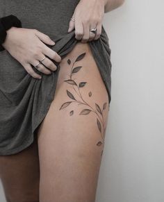 a woman is showing off her tattoo on the side of her thigh, which shows leaves