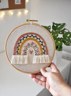 someone is holding up a small embroidery hoop with a rainbow in the middle and flowers on it