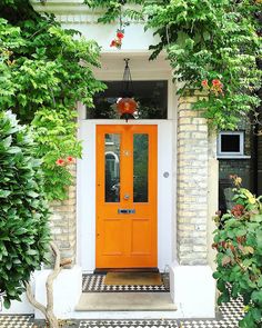 an orange front door surrounded by greenery