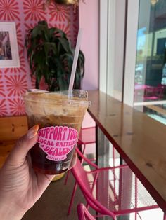 a person holding up a cup of coffee in front of a table with pink chairs