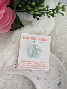 a white plate topped with a star shaped brooch on top of a table next to pink flowers