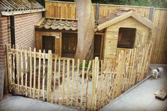 a dog house made out of wood with a fence around it and a cat in the yard