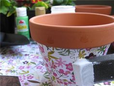 two flower pots sitting next to each other on top of a table with plants in the background