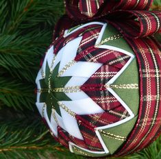 a christmas ornament hanging on a tree with red, green and white plaid ribbon