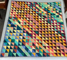 a multicolored quilt is displayed on a table with a chair in the background