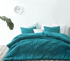 a bed with teal colored comforters and pillows in a white room next to a clock