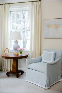 a chair and table in front of a window with drapes on the windowsill